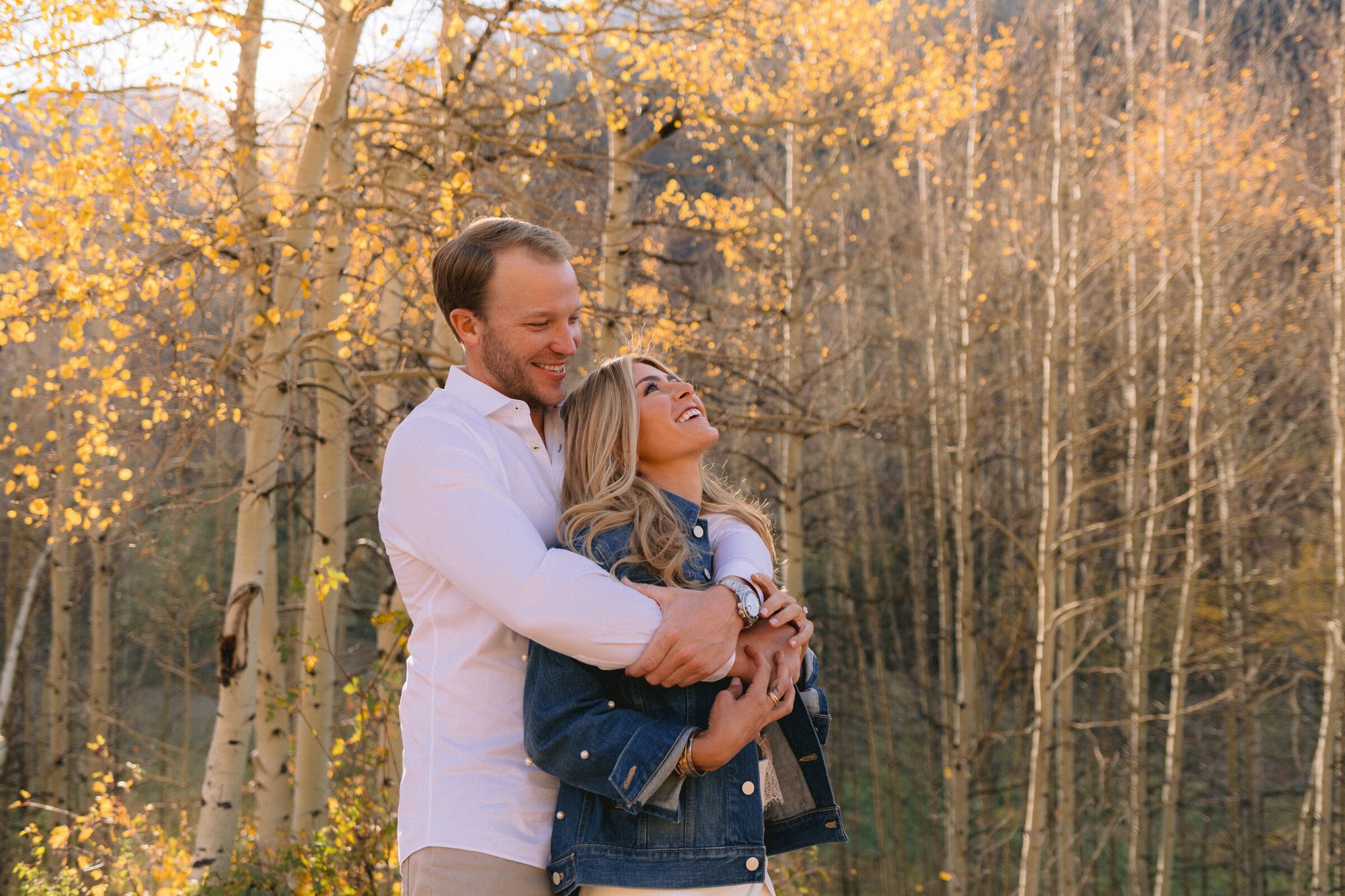 Couple embracing among golden aspen trees during fall engagement session in Colorado