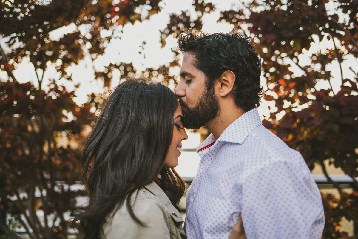Kavita and Amit sharing a kiss beneath autumn trees near the Brooklyn Bridge during their NYC engagement session by Marco Wang Photography