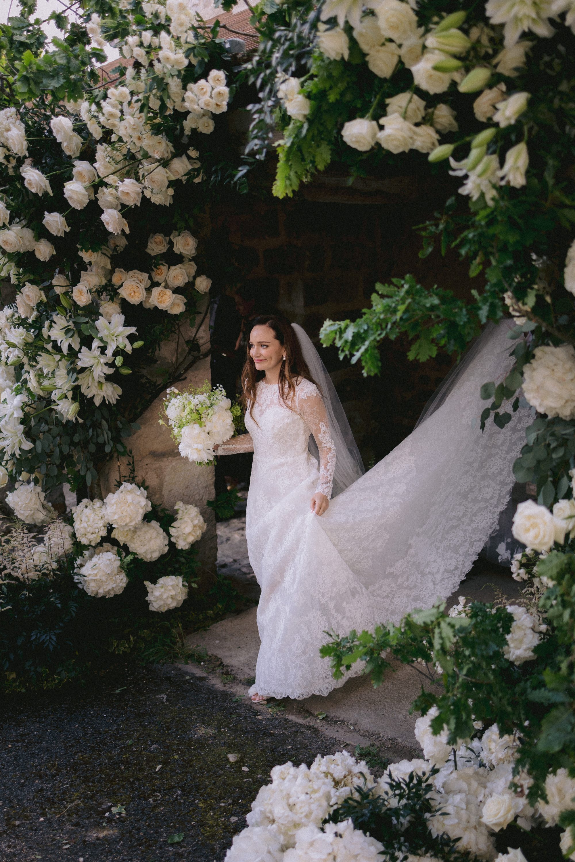 Bride under white floral archway at Chateau de Farcheville France destination wedding